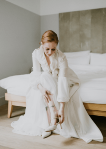 Bride sitting on a bed wearing a silk organza bridal coat